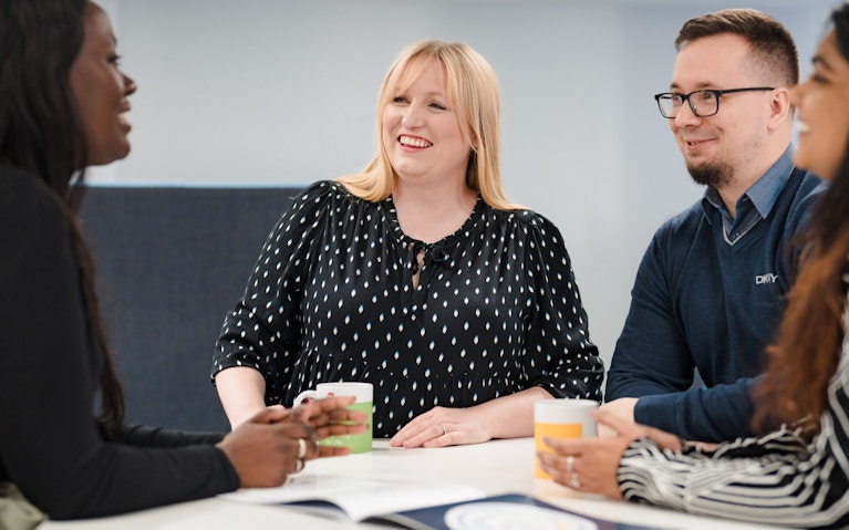 Four professionals sitting around a meeting table and smiling