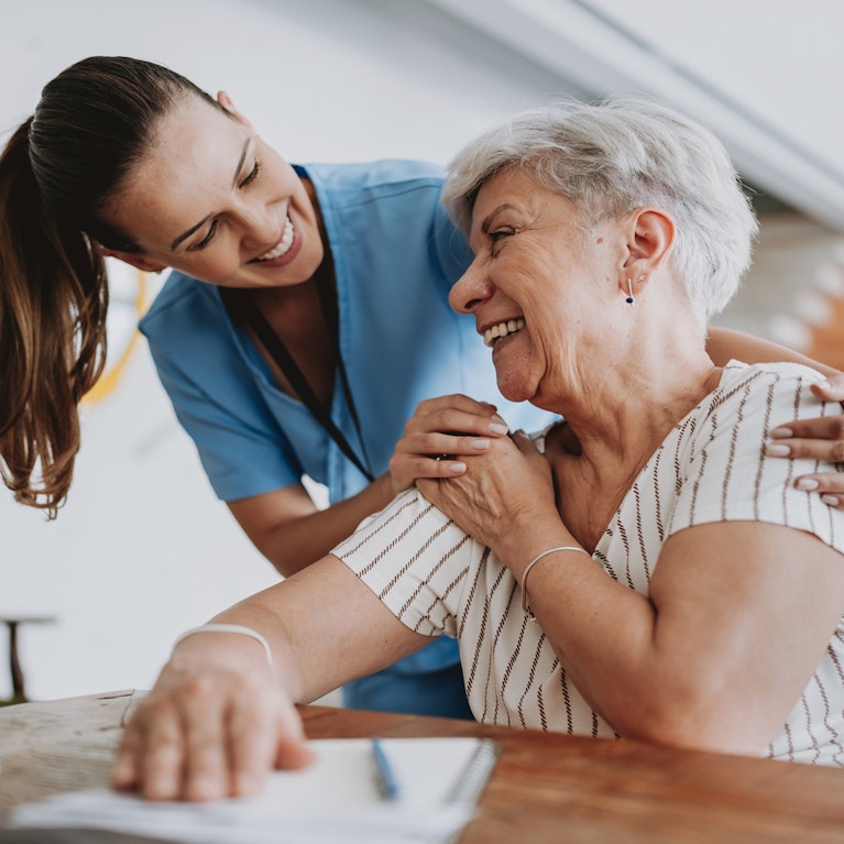 Home care healthcare professional with arms around smiling senior patient.