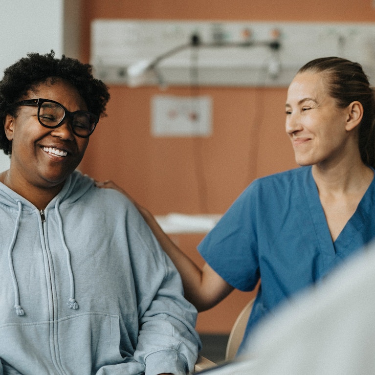 Smiling female nurse consoling happy patient sitting with doctor during consultation at hospital