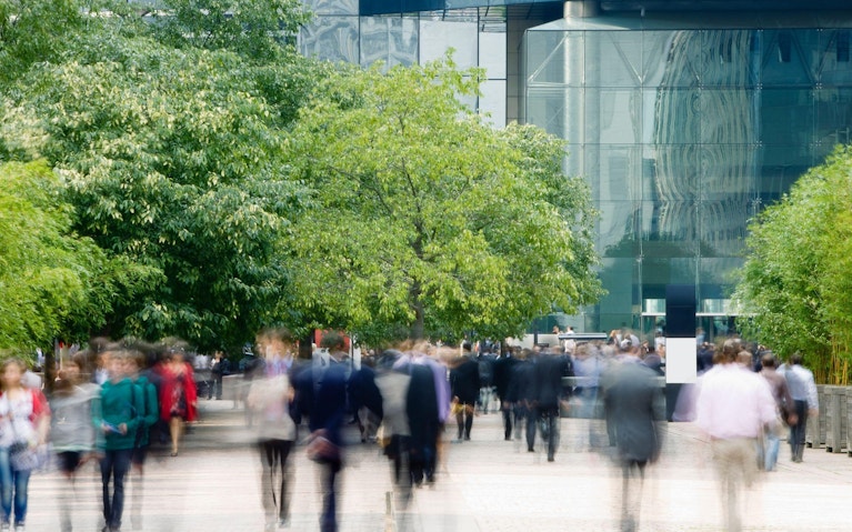 Blurred view of people walking towards office building in plaza with trees