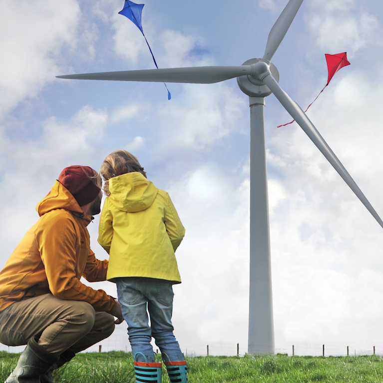 Parent and child flying kites by wind turbine